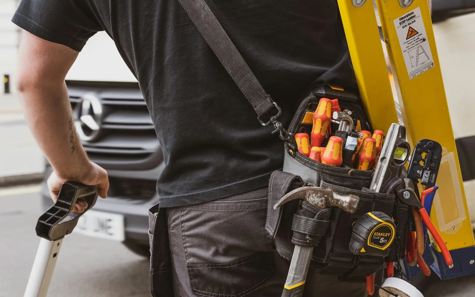 Artisan équipé de sa ceinture porte-outils devant son fourgon